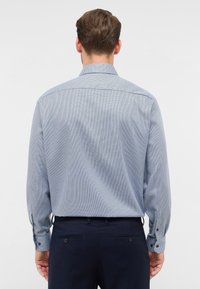 Camicia da uomo a maniche lunghe in azzurro chiaro con un motivo a quadri. Presenta polsini con bottone e colletto classico. Tessuto liscio con una vestibilità strutturata.