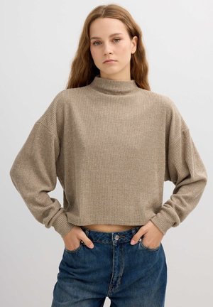 Suéter beige de cuello vuelto acanalado con mangas largas, de corte corto, combinado con jeans de mezclilla azul de tiro alto. Textura suave, ajuste relajado.
