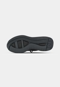 Semelle de chaussure noire avec des motifs de grip texturés et le mot BOSS embossé près de la zone des orteils sur un fond clair uni.