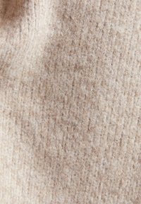Beige textiel met een zachte, geweven uitstraling, voorzien van een subtiel patroon en een pluizige afwerking, ideaal voor kleding of stoffering.