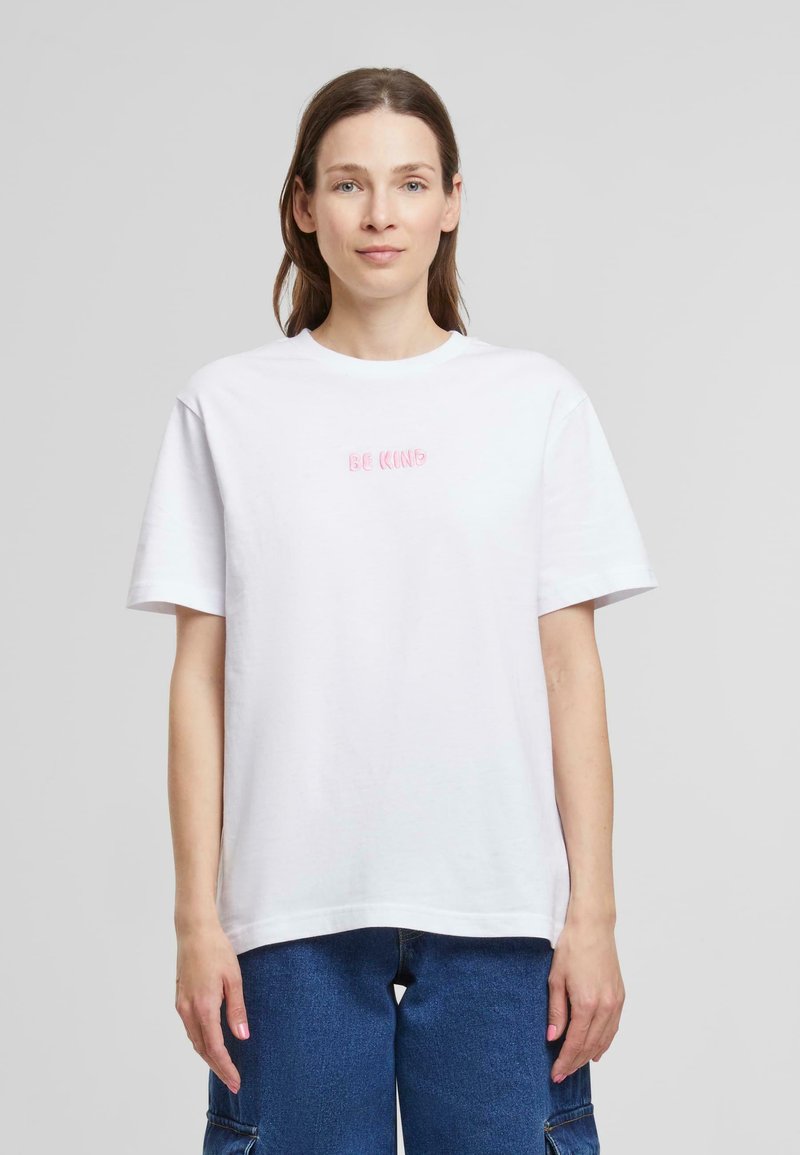 White cotton t-shirt with short sleeves featuring pink embroidered text "BE KIND" on the chest. Casual, relaxed fit.