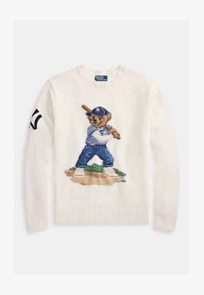 Λευκό πλεκτό πουλόβερ με κέντημα αρκούδας ντυμένης με στολή μπέιζμπολ, κρατώντας ένα ρόπαλο. Διαθέτει ριμπ μανσέτες και λαιμόκοψη.