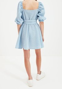 Modré kostkované šaty s krátkými nafouknutými rukávy, čtveratým výstřihem na zádech, staženým pasem a rozšířenou sukní. V kombinaci s bílými teniskami.