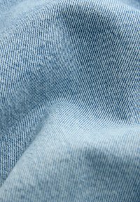 Detailní záběr světle modrého džínsového materiálu ukazující detailní texturu a diagonální vazbu s jemnými záhyby.