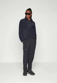 Fleece pullover in donker marineblauw met een halve rits, ritszakken, gecombineerd met donkere cargobroek en zwarte veterschoenen.