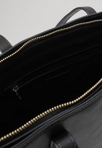 Fekete bőr kézitáska arany cipzárral, tágas belső térrel és több zsebbel a rendszerezéshez. Texturált felület és strapabíró fogantyúk.