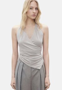 Svijetlosiva halter-top majica s drapiranim, omotanim dizajnom i mekanom teksturom, u kombinaciji s visoko strukiranim sivim plisiranim hlačama.