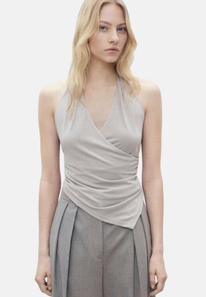 Top halter grigio chiaro con design drappeggiato e avvolgente e texture morbida, abbinato a pantaloni grigi a vita alta con pieghe.