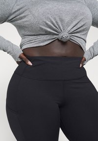 Gray long-sleeve top with a knotted detail at the waist paired with high-waisted black leggings featuring a smooth, stretchy fabric.