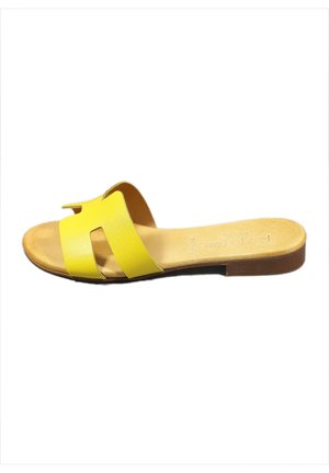 Gelbe Sandalen mit einem minimalistischen Design, die zwei breite Riemen und eine flache braune Sohle aufweisen. Das Material scheint glatt mit einer matten Oberfläche zu sein.