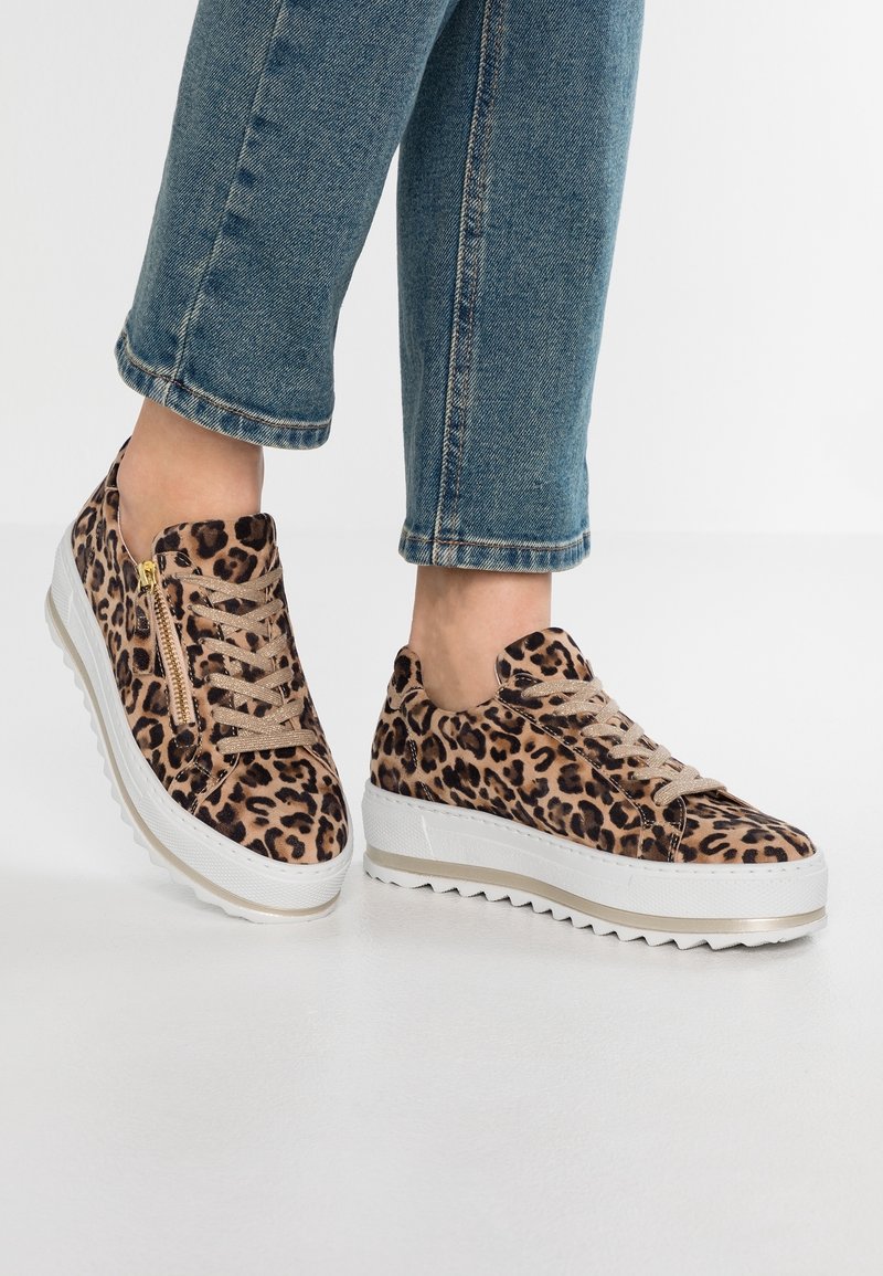 Les baskets à imprimé léopard présentent un dessus texturé, des lacets beiges, un détail de fermeture éclair sur le côté et une épaisse semelle plateforme blanche avec un accent doré.
