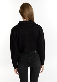 Maglione nero corto con scollatura a coste, visto da dietro. Abbinato a jeans neri a vita alta con tasche posteriori.