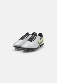 Silver soccer cleats with a textured design, black laces, and a bright yellow Nike swoosh logo. Multi-directional studs on the outsole.