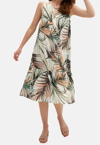 Une robe sans manches avec un motif de feuilles tropicales en vert, orange et blanc. La robe a un ourlet en étages et une coupe ample.