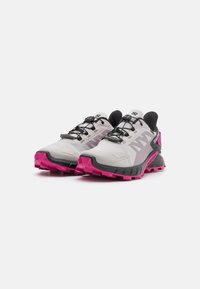 Scarpe da trail running con una tomaia grigio chiaro, accenti neri e suola rosa. Suola tassellata per una migliore aderenza e sistema di allacciatura integrato.
