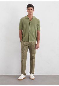 Short-sleeve, button-up shirt in light green textured fabric; paired with light tan pants and white sneakers with a beige sole.