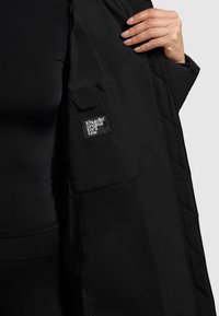 Giacca nera trapuntata dal design elegante, con una tasca a toppa sulla manica e un tessuto liscio. Accenti minimalisti ne esaltano l'aspetto.