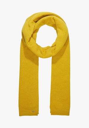 Gele wollen sjaal, gevouwen in een lus met twee rechte uiteinden, gebreide textuur en een klein rechthoekig metalen label bij één uiteinde.