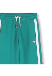 Τιρκουάζ παντελόνια φόρμας με ελαστική μέση και κορδόνι, λευκές πλευρικές ρίγες και ροζ λεπτομέρειες. Διαθέτουν μικρό λογότυπο στην εμπρόσθια αριστερή τσέπη. Μαλακή υφή υφάσματος.