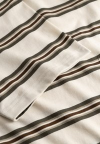 Tissu en coton avec des rayures ondulées alternées en beige, marron et olive. Caractérisé par une texture douce et des coutures soignées le long des bords.