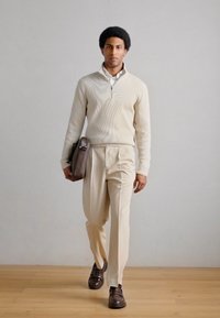 Beige genser med glidelås, kremfargede bukser, brune skinnsko og en mørkebrun veske. Glatte teksturer og minimalistisk design.