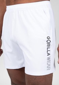 Witte sportshorts met een elastische tailleband, voorzien van een zwart "GORILLA WEAR" logo dat verticaal aan de linkerkant is gedrukt. Zachte textuur.