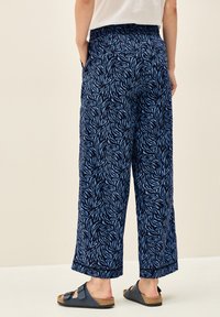 Marinblå vida byxor med ett ljust bl�ått bladmönster, med resårmidja och sidofickor. Bärs med svarta sandaler.