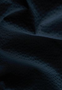 Tejido texturizado de un azul marino oscuro con un sutil patrón perforado, que muestra suaves pliegues ondulados. La superficie parece lisa pero está llena de detalles.