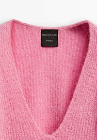 Różowy sweter w serek, wyróżniający się miękką, puszystą teksturą i prążkowanymi detalami, z czarną metką z napisem "Massimo Dutti Studio."