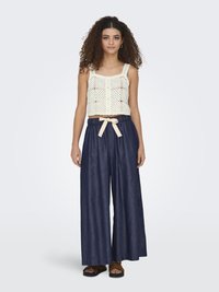 Gehaakte cropped top in ivoorkleur met een vierkante halslijn en knoopdetails, gecombineerd met donkerkleurige wijde broek met lichtgewicht stof en beige ceintuur.