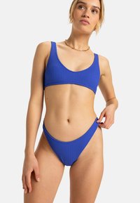 Blue ribbed bikini in a sporty design featuring a scoop neckline and high-cut bottoms, highlighting textured fabric and a minimalistic style.