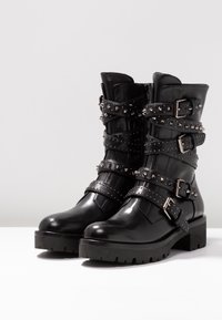 Czarne skórzane botki z kilkoma paskami ozdobionymi ćwiekami, srebrnymi klamrami oraz masywną, teksturowaną podeszwą. Gładka powierzchnia z projektem zaokrąglonych palców.