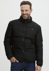 Črn puhovka z visokim ovratnikom, z sprednjim zadrgo, stranskimi žepi in elastičnimi manšetami. Rdeča, bela in modra logotipna potiska na prsih.