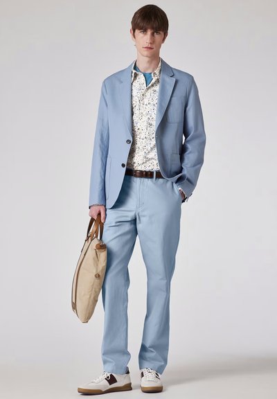 Giacca e pantaloni di seta azzurro chiaro, camicia floreale, cintura marrone, borsa beige, sneakers bianche e marroni. Tessuto morbido, vestibilità moderna, look casual.
