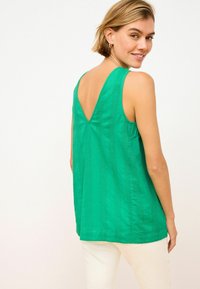 Top verde senza maniche con scollatura a V, realizzato in tessuto strutturato e con righe verticali, abbinato a pantaloni bianchi.
