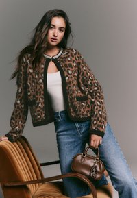 Leopardi-kuvioitu neuletakki ruskeana ja mustana, jossa on jalokivikoristeinen kaulus. Yhdistetty korkeavyötäröisiin sinisiin farkkuihin ja ruskeaan käsilaukkuun.