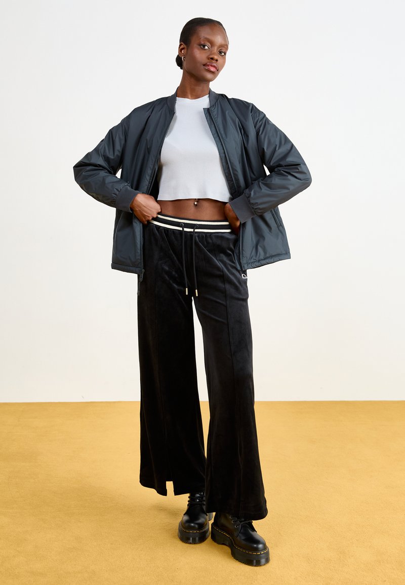 Ciemnoszara kurtka bomberka noszona na dopasowanej białej crop topie, w połączeniu z czarnymi welurowymi spodniami typu wide-leg z prążkowanym pasem i masywnymi czarnymi botkami.