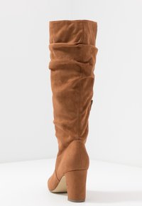 Botte marron décontractée hauteur genoux en daim souple, avec un talon épais et un design incurvé en haut. Présente des coutures le long des coutures.