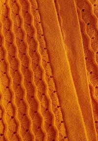 Tejido de punto brillante en color naranja que presenta un patrón de olas texturizado y una franja suave y contrastante. Textura suave con pequeños agujeros a lo largo del diseño.