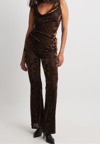 Brauner floraler Samt-Overall mit drapiertem Ausschnitt, tailliertem Oberteil und weitem Bein. Besitzt eine glatte Textur und goldfarbene Akzente.