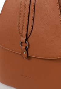 Sac en cuir marron avec une finition texturée, équipé d'un fermoir circulaire en argent et de coutures noires contrastantes le long des bords.