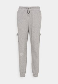 Grå joggerbyxor i mjukt tyg, med dragsko i midjan, sidofickor i cargo-stil och tryckt textdetalj nära fållen. Elastiska muddar.