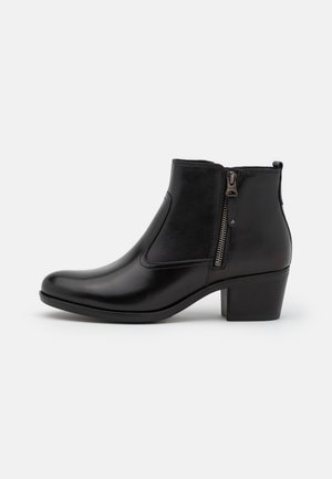 Bottine en cuir noir avec fermeture éclair latérale, talon bloc bas et bout arrondi sur fond gris clair uni.