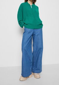 Grön zip-up stickad tröja med rund halsringning, matchad med vida ljusblå jeans och beige klackstövlar med tjock sula.