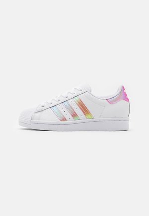 Hvid lavtop sneaker med iriserende tre striber og lyserød hælkappe, snørelukning og tekstureret gummi tåhætte.