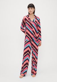 Multifarget chevron-mønsteret pyjamas sæt i pink, blå og mørk lilla, med en knaplukket skjorte og løst fitting bukser. Fremstillet af bomuldsstof.