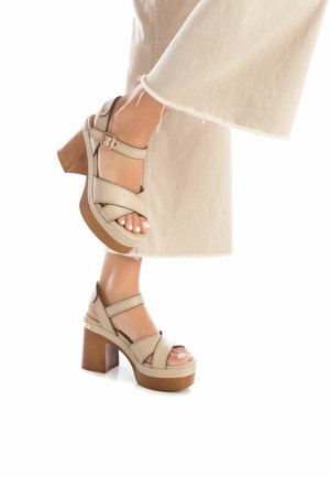 Sandali platform beige con cinturini incrociati, punta aperta e fibbia alla caviglia. Tacco spesso marrone con una superficie liscia e dettagli accentuati delicati.