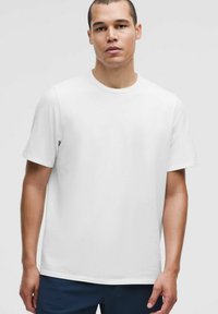 Balts īsām piedurknēm T-krekls ar apaļu kakla izgriezumu, izgatavots no gludas auduma; ar brīvu piegriezumu un bez redzamām detaļām vai zīmējumiem.