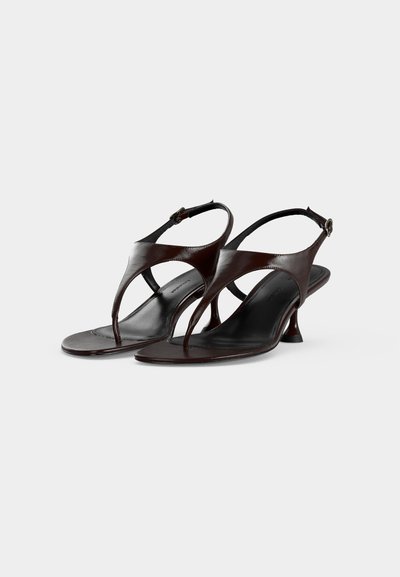 Ciemnobrązowe skórzane sandały typu slingback z paskami między palcami, małymi rozszerzanymi obcasami i regulowanymi zapięciami na klamrę na białym tle.