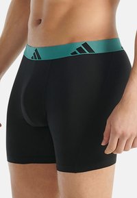 Czarne bokserki z morsko-zielonym pasem w talii z czarnymi akcentami logo, dopasowany krój i gładka faktura tkaniny.